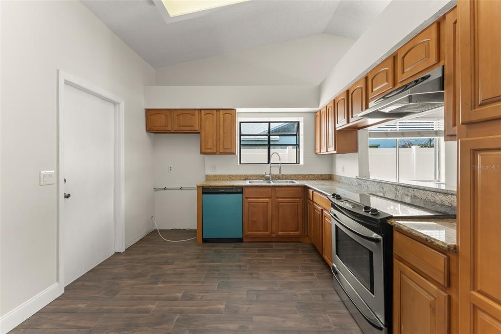 A kitchen features wood cabinets, granite countertops, stainless steel appliances, and dark wood-look flooring — 2458 LONG MEADOW WAY, ORLANDO, FL