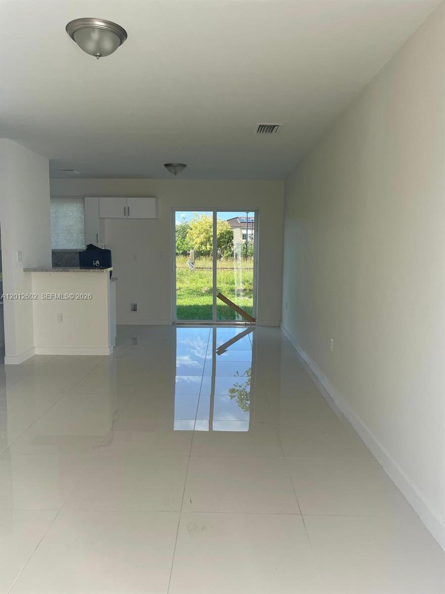 An open-concept living area features white tile floors, a kitchen counter, and sliding glass doors — 2121 NW 72nd St # 2121, Miami FL 33147, MIAMI, FL