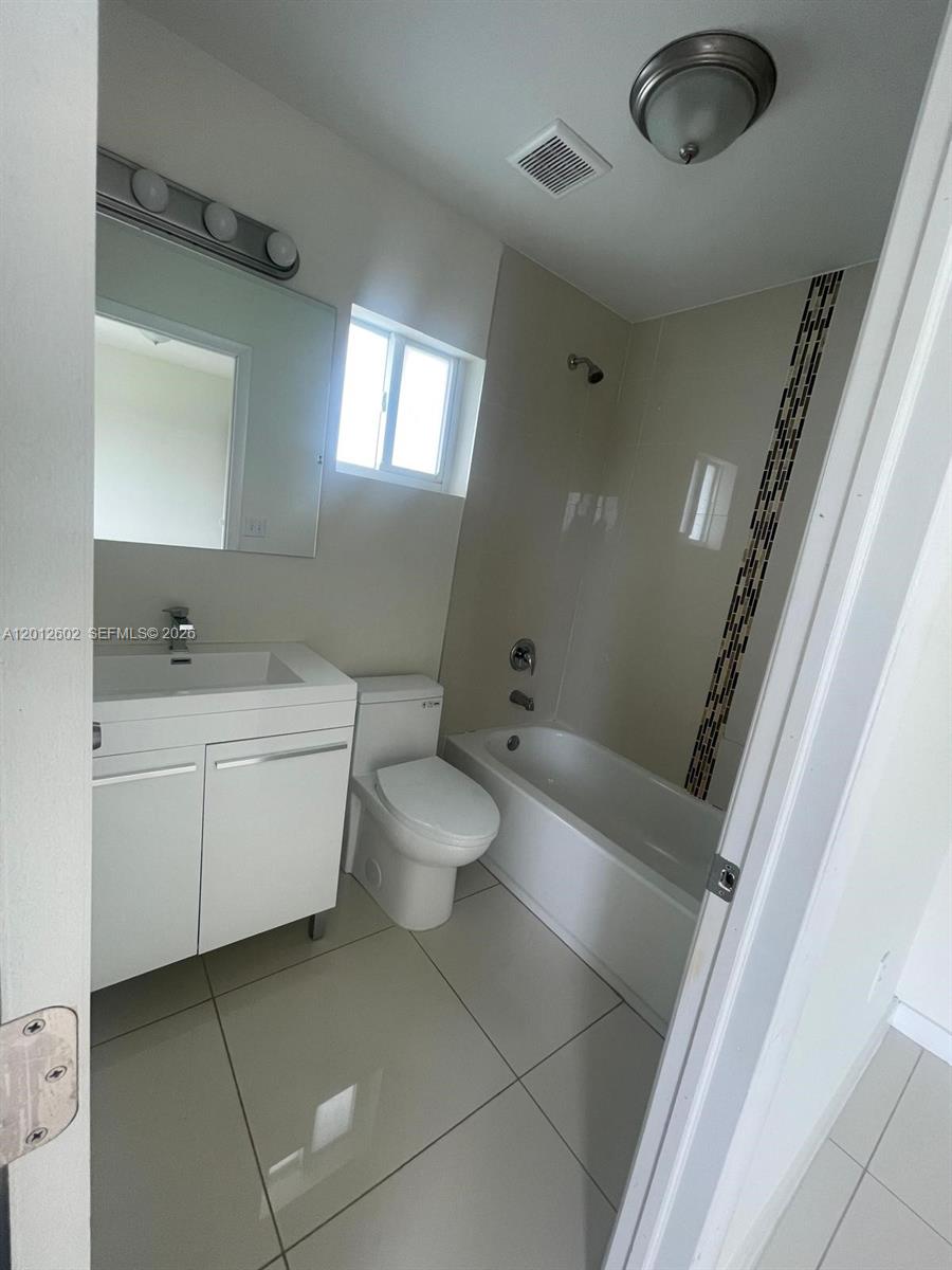 A bathroom features a white vanity, a toilet, and a bathtub with tiled walls — 2121 NW 72nd St # 2121, Miami FL 33147, MIAMI, FL