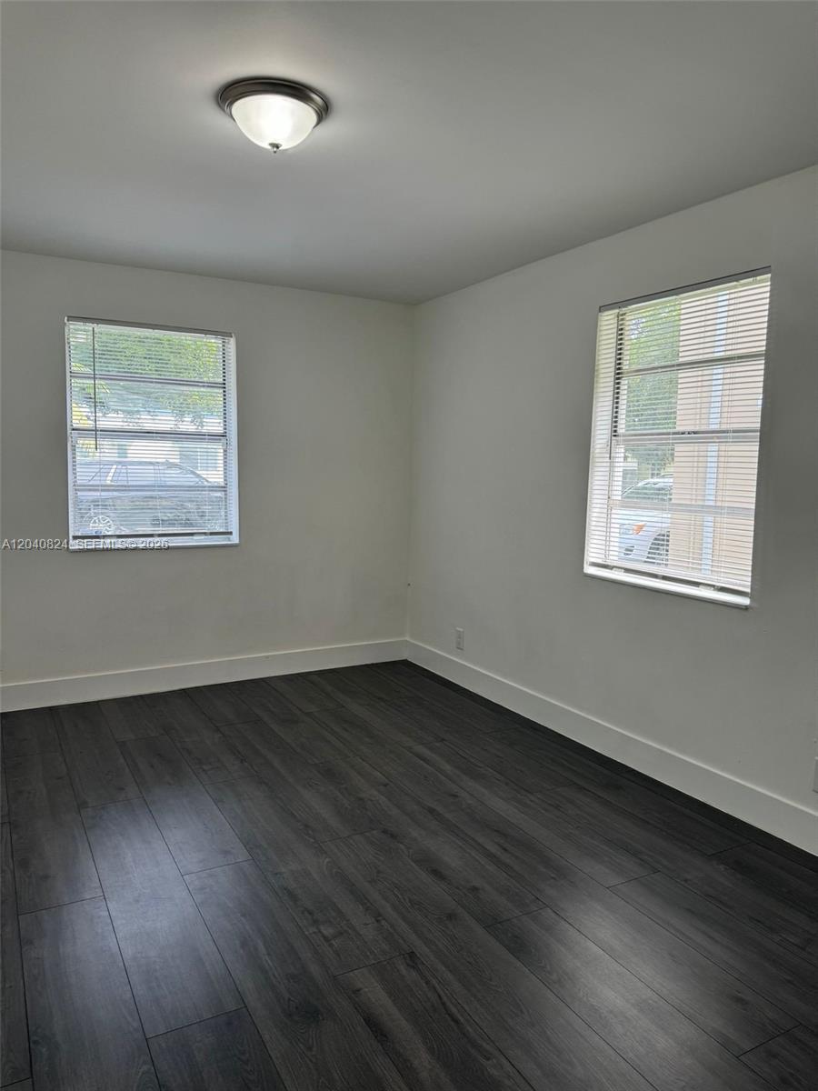 An empty bedroom features white walls, dark wood-look flooring, and two windows with blinds — 1842 Madison St # 2, Hollywood FL 33020, HOLLYWOOD, FL