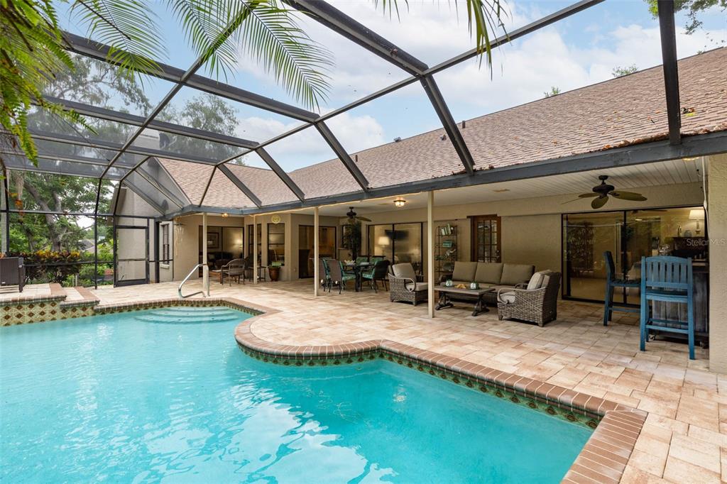 A screened-in patio features a swimming pool, stone pavers, and outdoor furniture — 1056 ENISWOOD PKWY, PALM HARBOR, FL