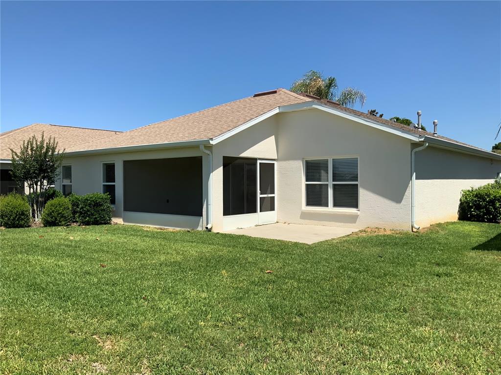 The back exterior of a single-story house features a screened-in porch and a concrete patio — 27215 ROANOKE DRIVE, LEESBURG, FL