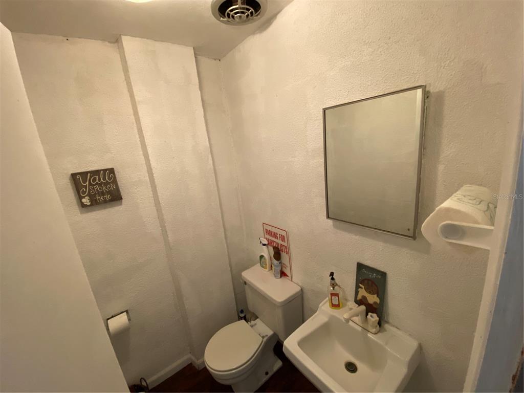 A small bathroom features a toilet, a wall-mounted sink, a mirror, and textured white walls — 207 N SCENIC HIGHWAY UNIT 207 & 211, FROSTPROOF, FL