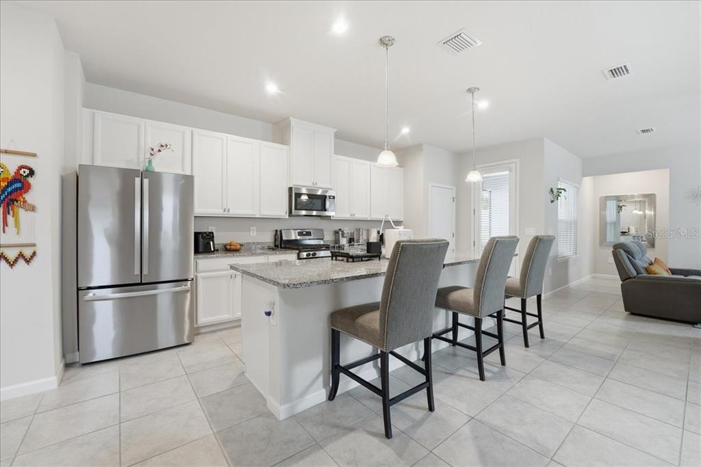 A kitchen features white cabinets, stainless steel appliances, granite countertops, and a breakfast bar — 3979 CAPITAL REEF WAY, APOPKA, FL