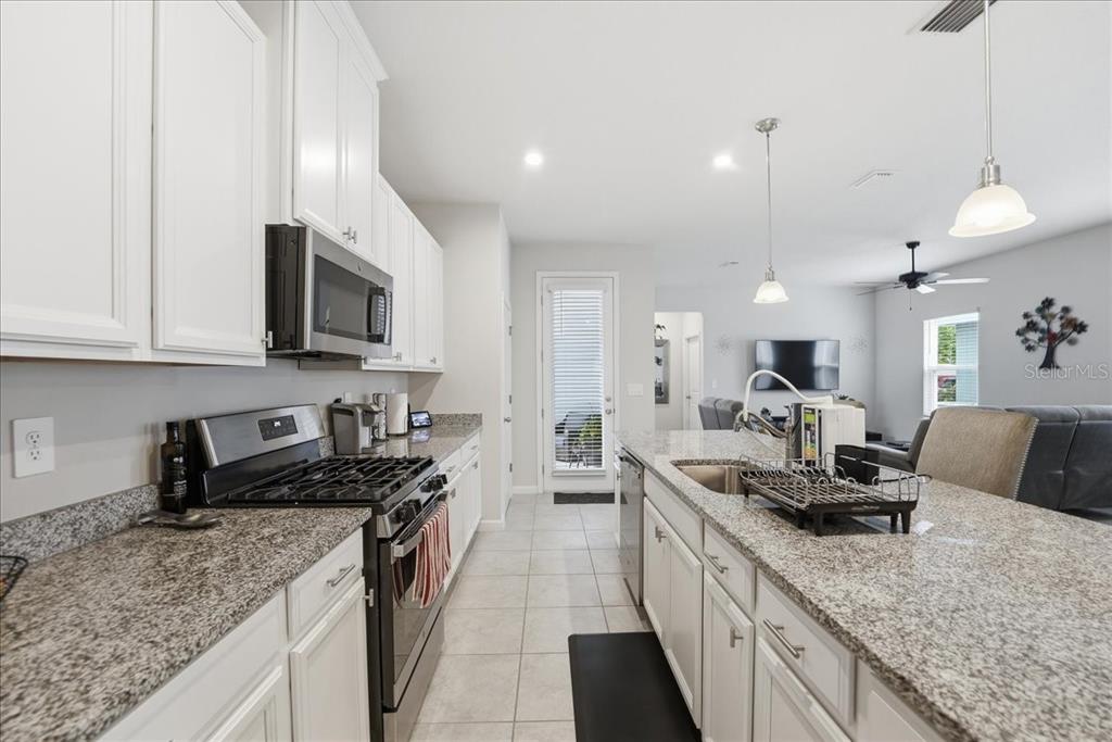A kitchen features white cabinets, granite countertops, stainless steel appliances, and an island with seating — 3979 CAPITAL REEF WAY, APOPKA, FL