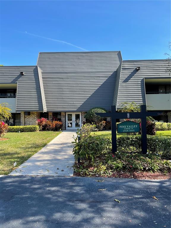 A sidewalk leads to the entrance of a two-story building with gray siding — 36750 US HIGHWAY 19 N UNIT 19-115, PALM HARBOR, FL