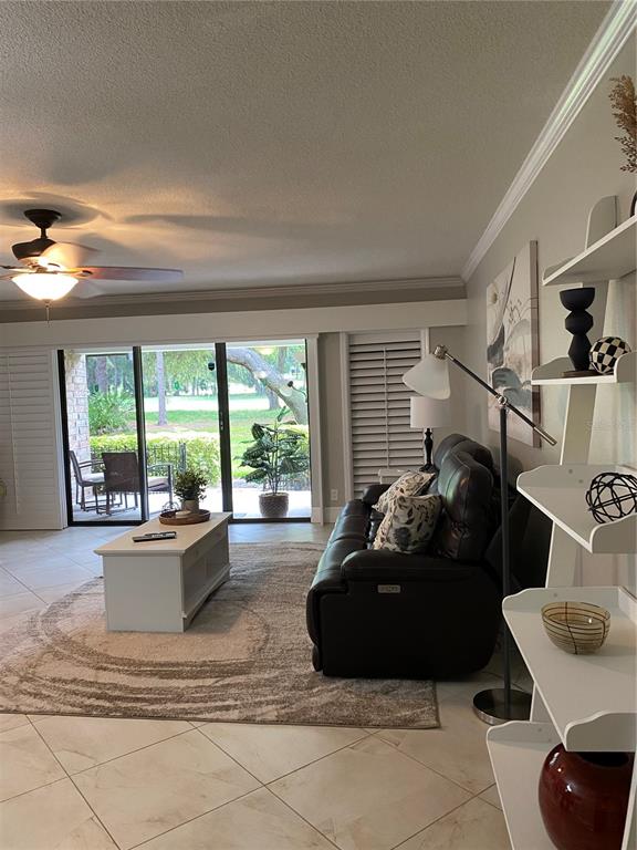 A living room features tile floors, a dark leather sofa, and sliding glass doors to a patio — 36750 US HIGHWAY 19 N UNIT 19-115, PALM HARBOR, FL
