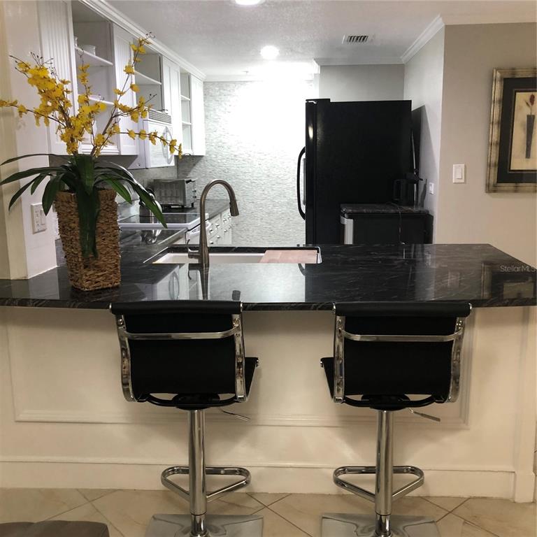 A kitchen features a black marble breakfast bar with two stools and white cabinetry — 36750 US HIGHWAY 19 N UNIT 19-115, PALM HARBOR, FL