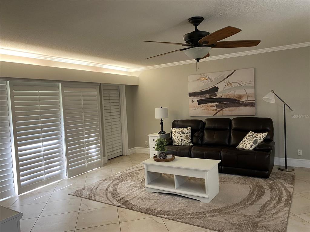 A living room features a dark leather sofa, white coffee table, and plantation shutters — 36750 US HIGHWAY 19 N UNIT 19-115, PALM HARBOR, FL