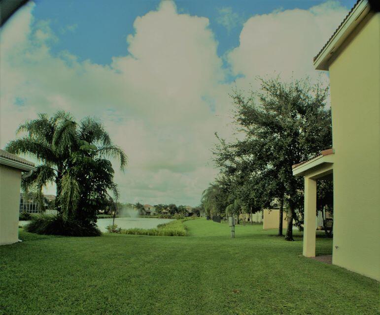 A grassy backyard features a palm tree, a small pond with a fountain, and houses — 8887 Chestnut Ridge Way, Boynton Beach FL 33473, BOYNTON BEACH, FL