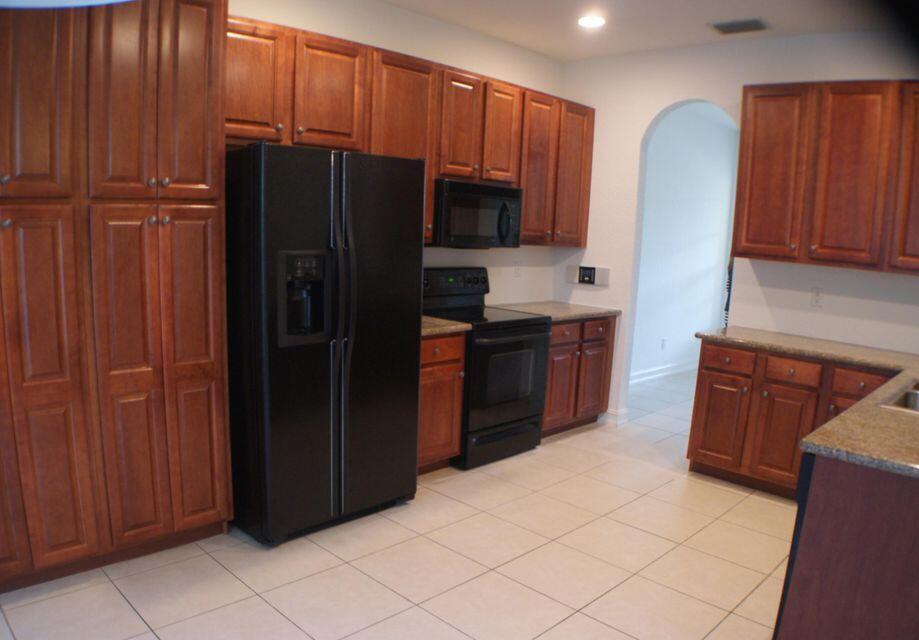 A kitchen with wood cabinets, black appliances, granite countertops, and light-colored tile flooring — 8887 Chestnut Ridge Way, Boynton Beach FL 33473, BOYNTON BEACH, FL