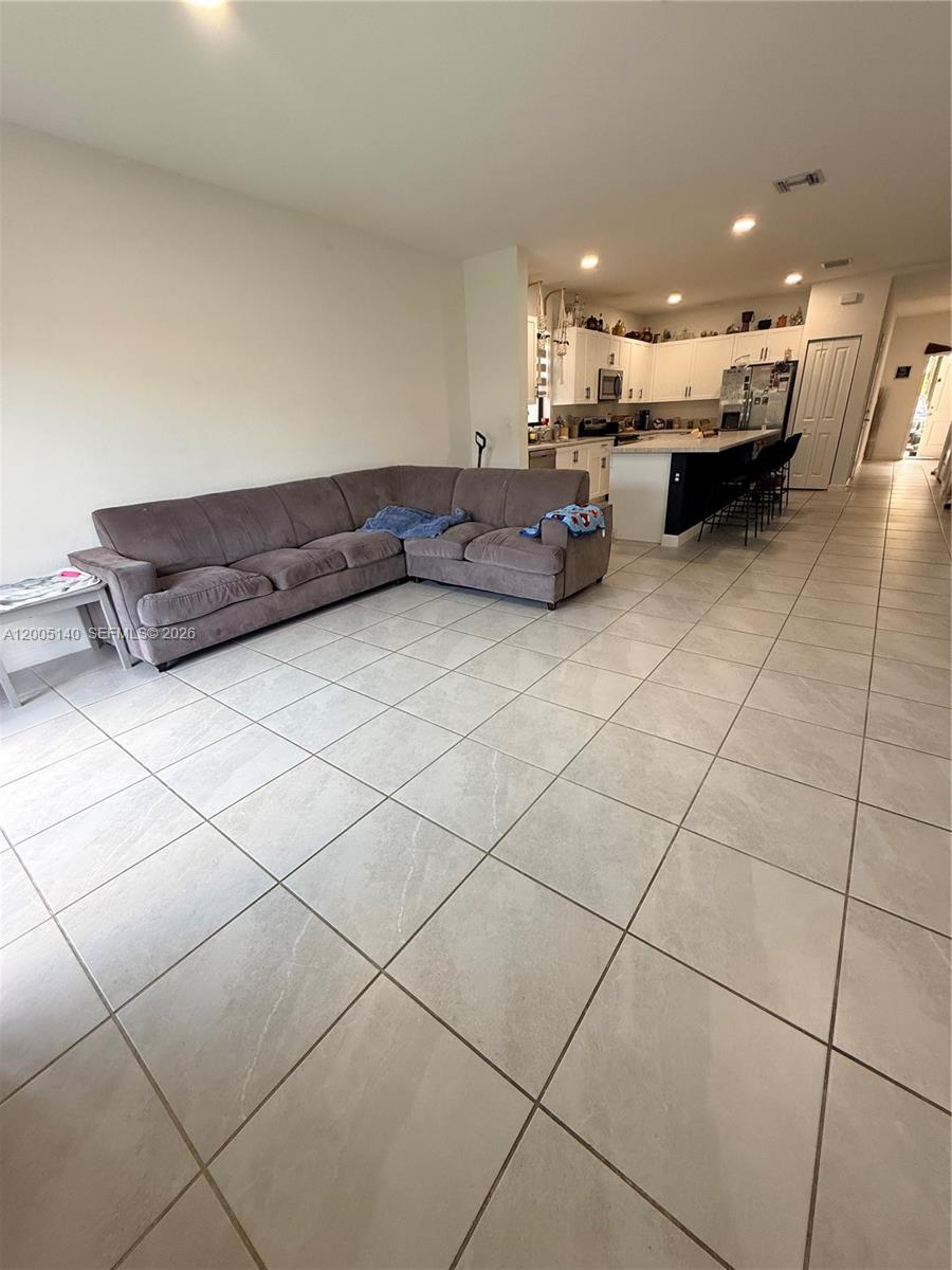 This open-concept living area features a large sectional sofa and a kitchen with white cabinets — 25441 SW 109th Ave, Homestead FL 33032, HOMESTEAD, FL