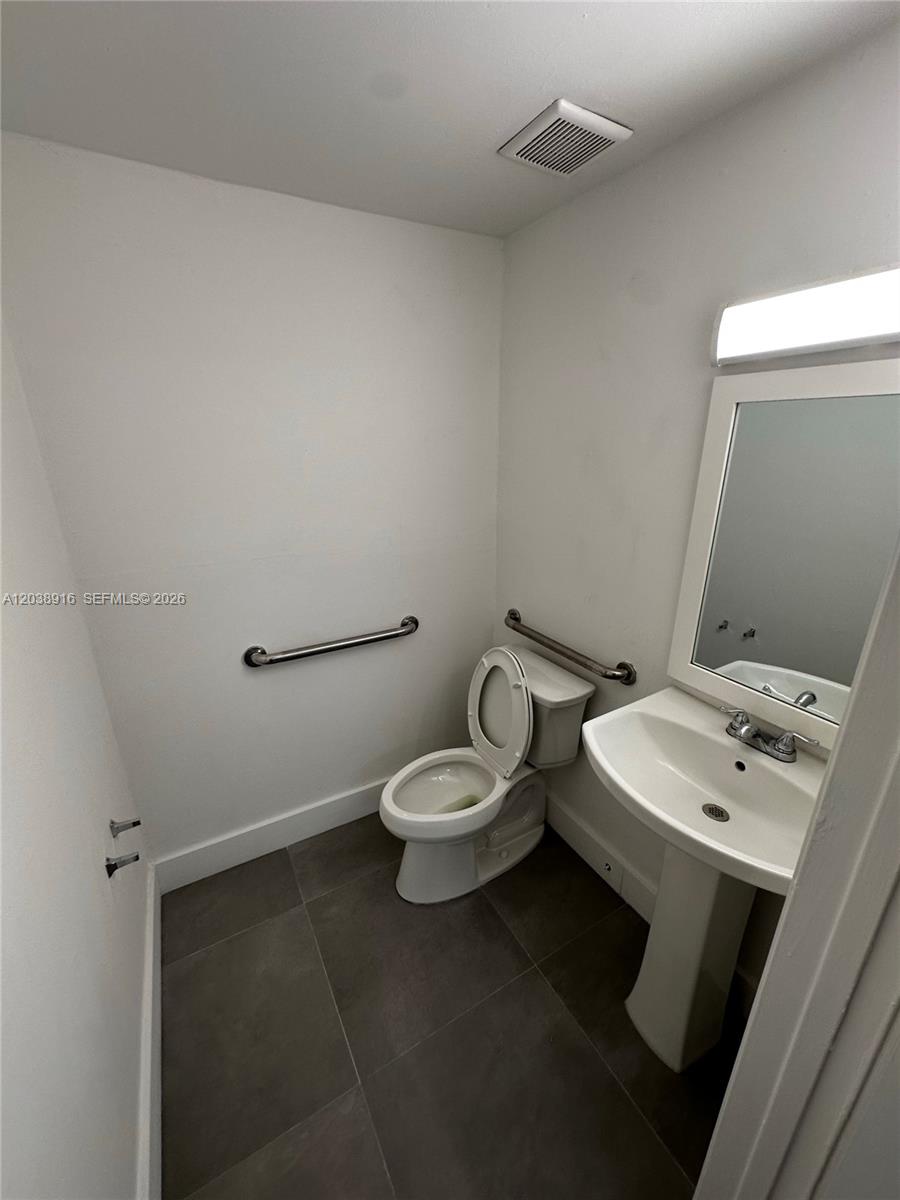 A small bathroom features a pedestal sink, a toilet with grab bars, and tiled flooring — FL
