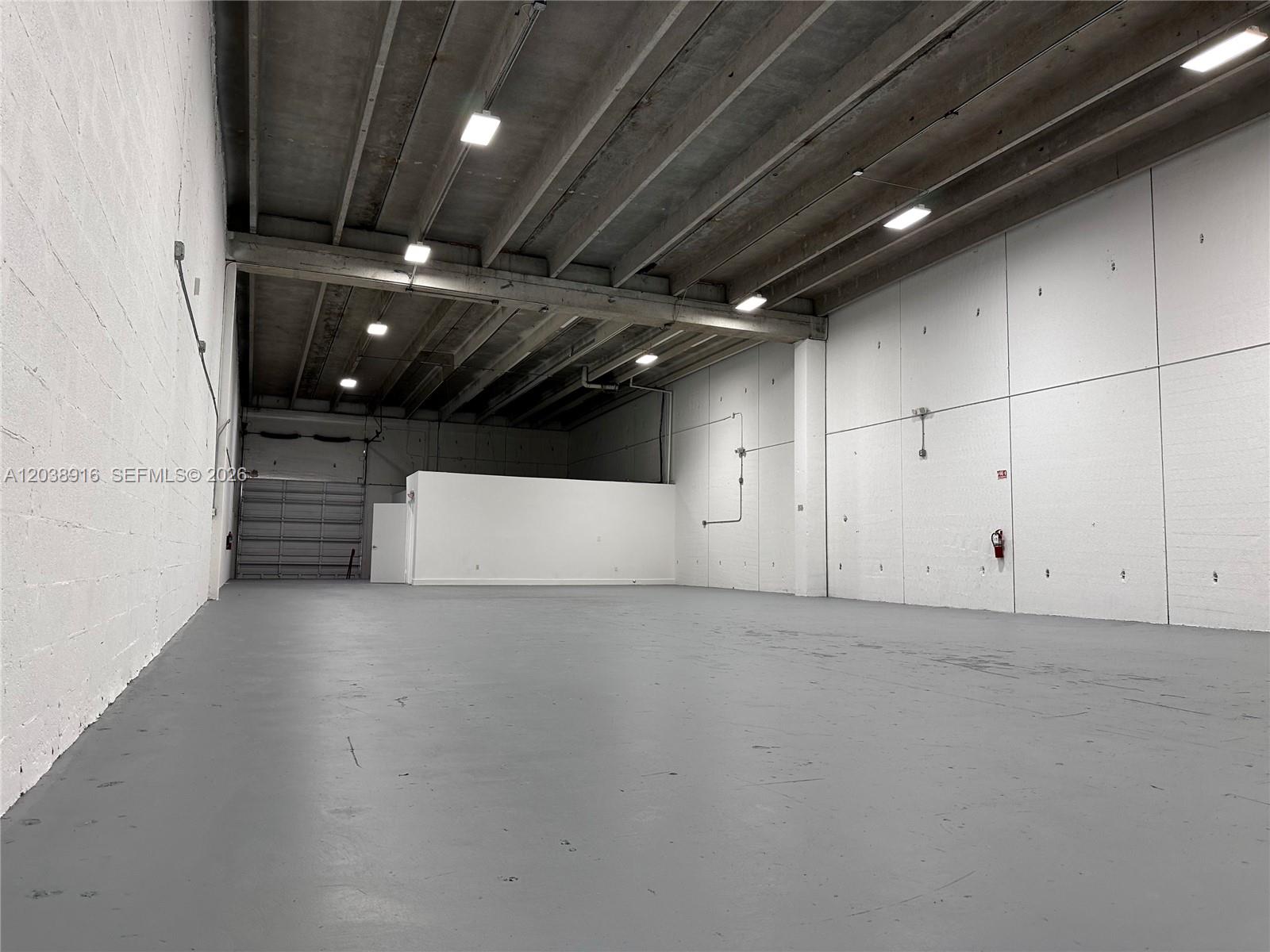 An empty warehouse space features high ceilings, exposed concrete beams, and gray painted floors — FL