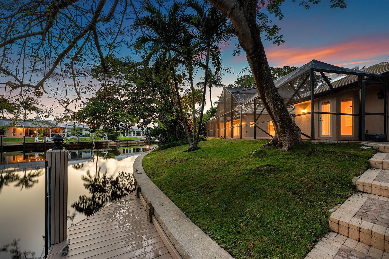 A waterfront home with a screened-in pool enclosure, a wooden dock, and a grassy lawn — 770 Peachtree Lane, Boca Raton FL 33486, BOCA RATON, FL