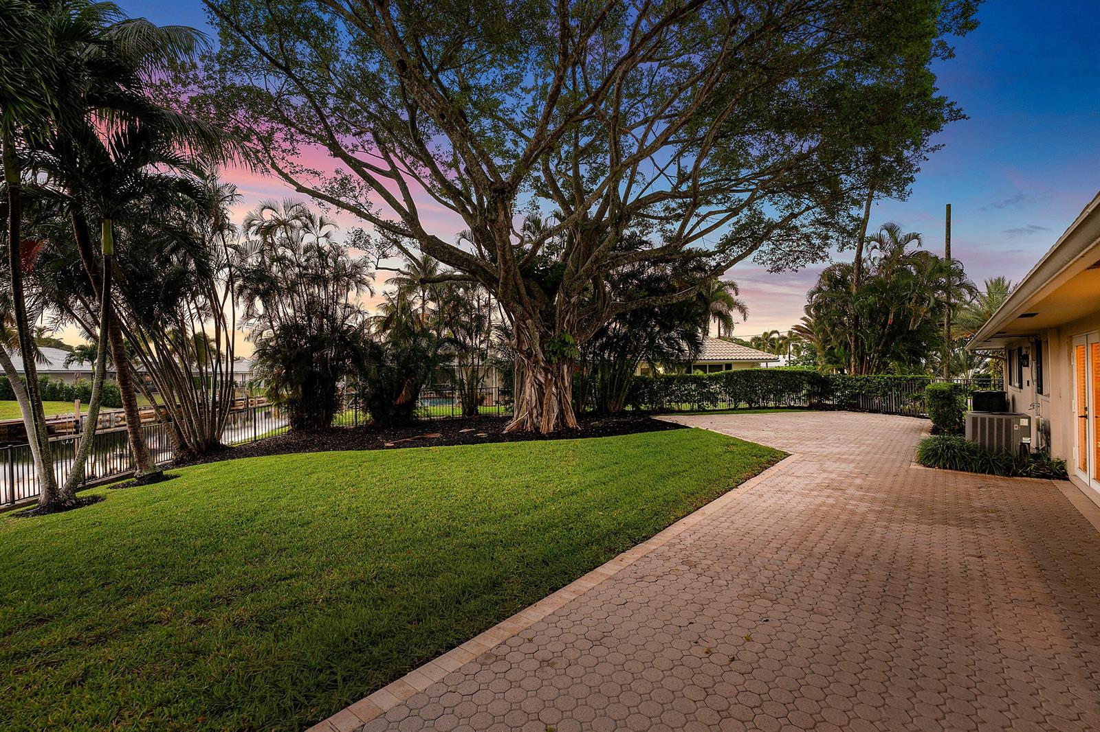 A large tree stands in a grassy backyard next to a paved patio and canal — 770 Peachtree Lane, Boca Raton FL 33486, BOCA RATON, FL