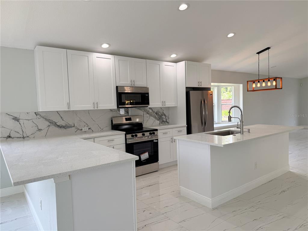 A modern kitchen features white cabinets, marble-patterned backsplash, quartz countertops, and stainless steel appliances — 9067 HASTINGS BEACH BOULEVARD, ORLANDO, FL
