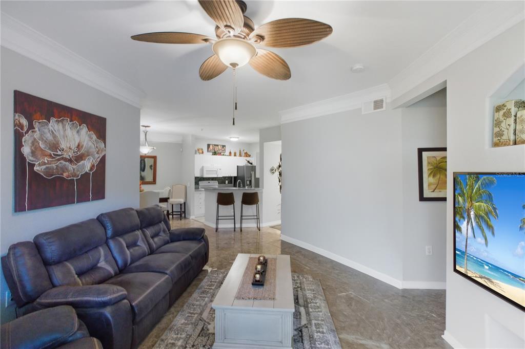 A living room with a dark sofa, coffee table, ceiling fan, and open kitchen beyond — 5122 NORTHRIDGE ROAD UNIT 107, SARASOTA, FL