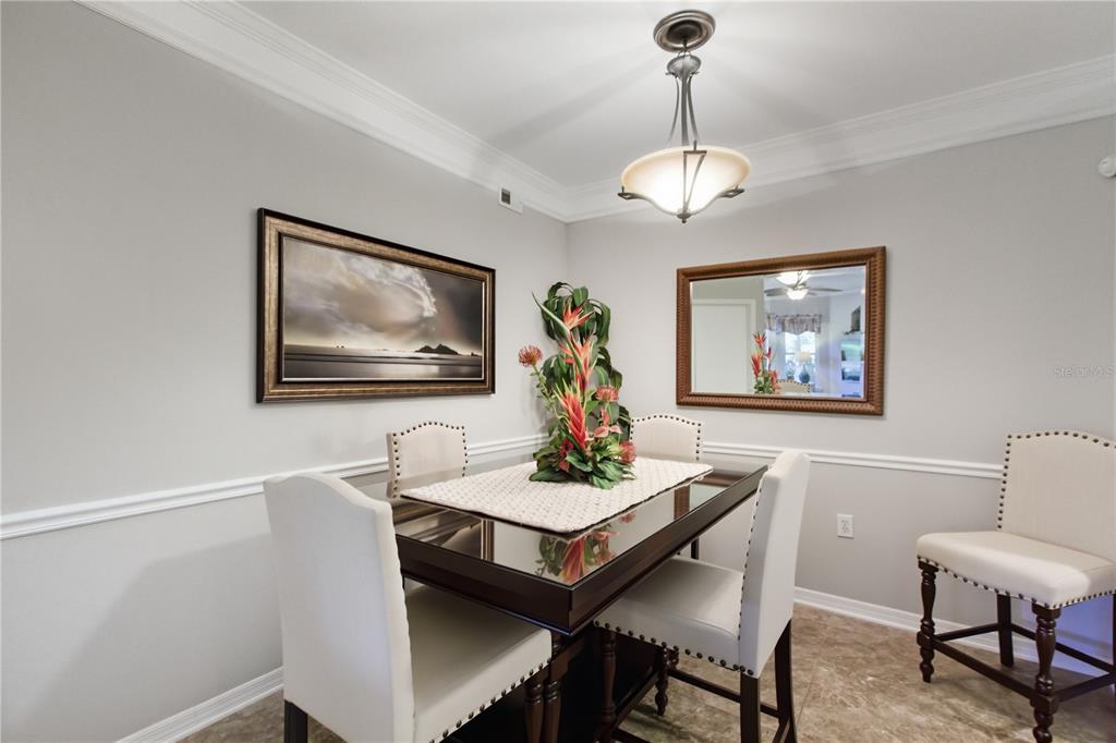 A dining room with a glass-topped table, four upholstered chairs, a mirror, and wall art — 5122 NORTHRIDGE ROAD UNIT 107, SARASOTA, FL