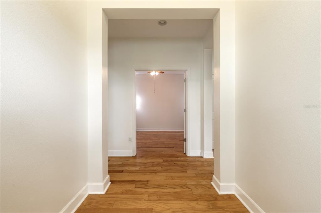 A hallway with hardwood floors leads through a doorway into another room with a fan — 544 LOST SHAKER WAY, DAYTONA BEACH, FL