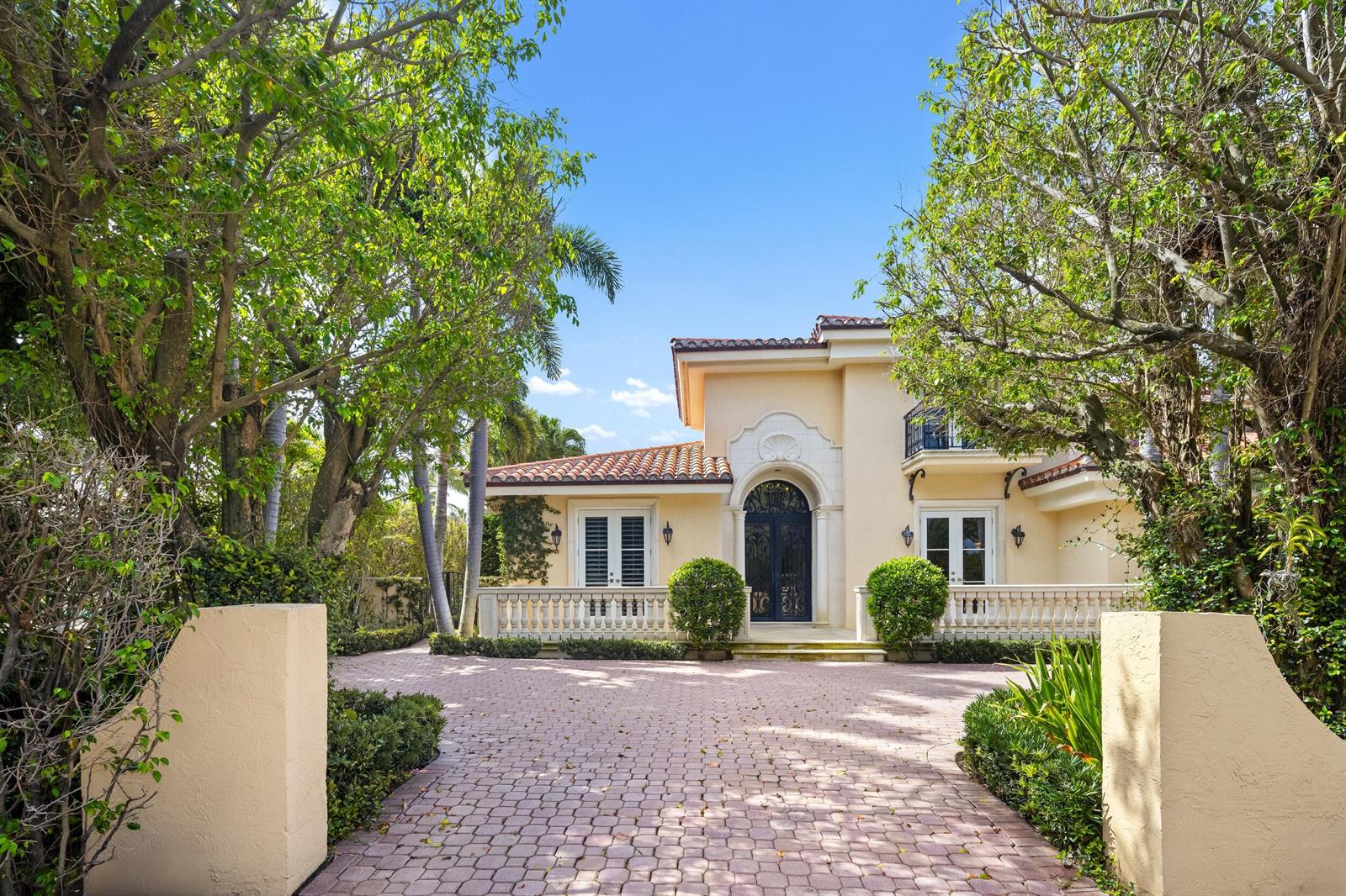 A two-story Mediterranean-style house with a paved driveway, arched entryway, and lush surrounding trees — 1460 N Ocean Boulevard, Palm Beach FL 33480, PALM BEACH, FL
