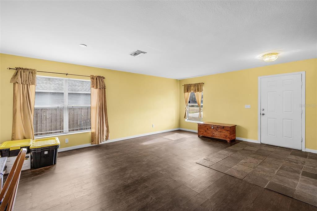 A living room with yellow walls, dark wood-look flooring, a tiled entryway, and two windows — 2496 WURTSMITH, NORTH PORT, FL