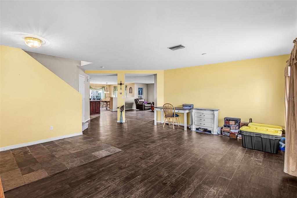A spacious room with yellow walls, dark wood-look flooring, and a desk area — 2496 WURTSMITH, NORTH PORT, FL