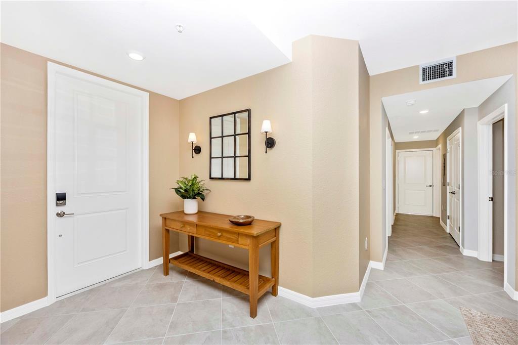 An entryway features a white door, a wooden console table, wall sconces, and tiled flooring — 17740 BORACAY COURT UNIT 102, VENICE, FL