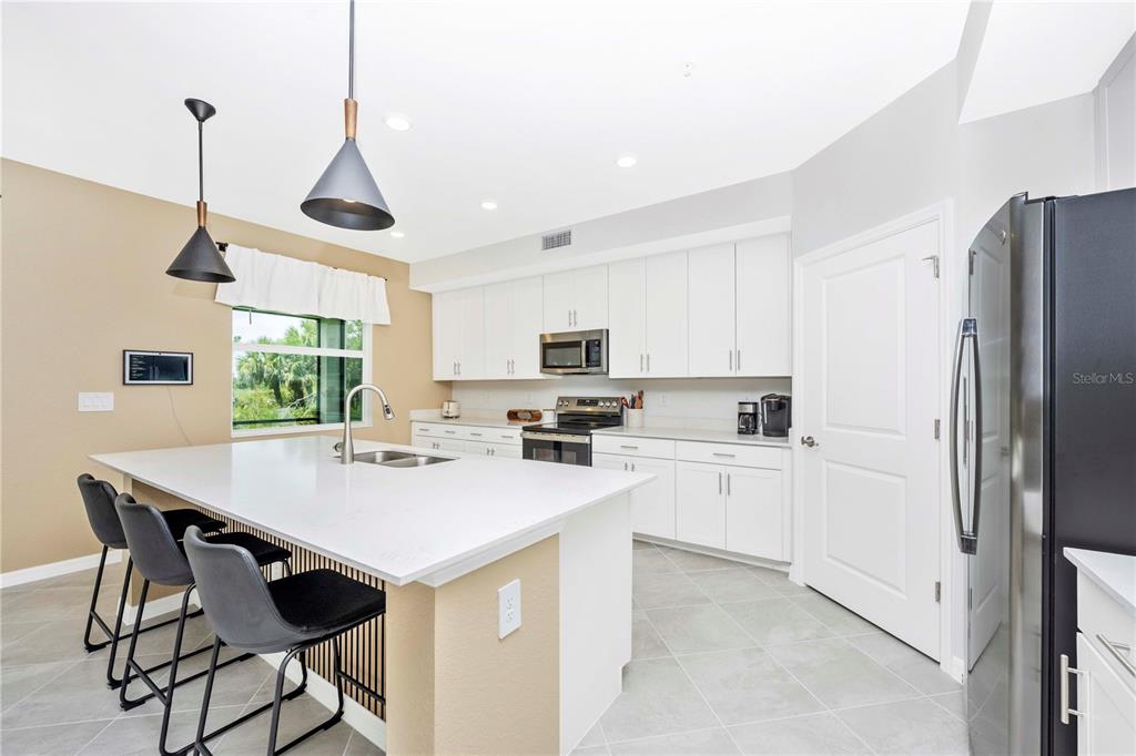 A modern kitchen features white cabinetry, a large quartz island with bar seating, and stainless appliances — 17740 BORACAY COURT UNIT 102, VENICE, FL
