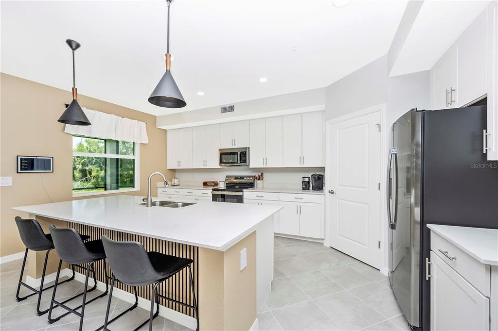 A modern kitchen features white cabinetry, a large island with bar seating, and stainless appliances — 17740 BORACAY COURT UNIT 102, VENICE, FL