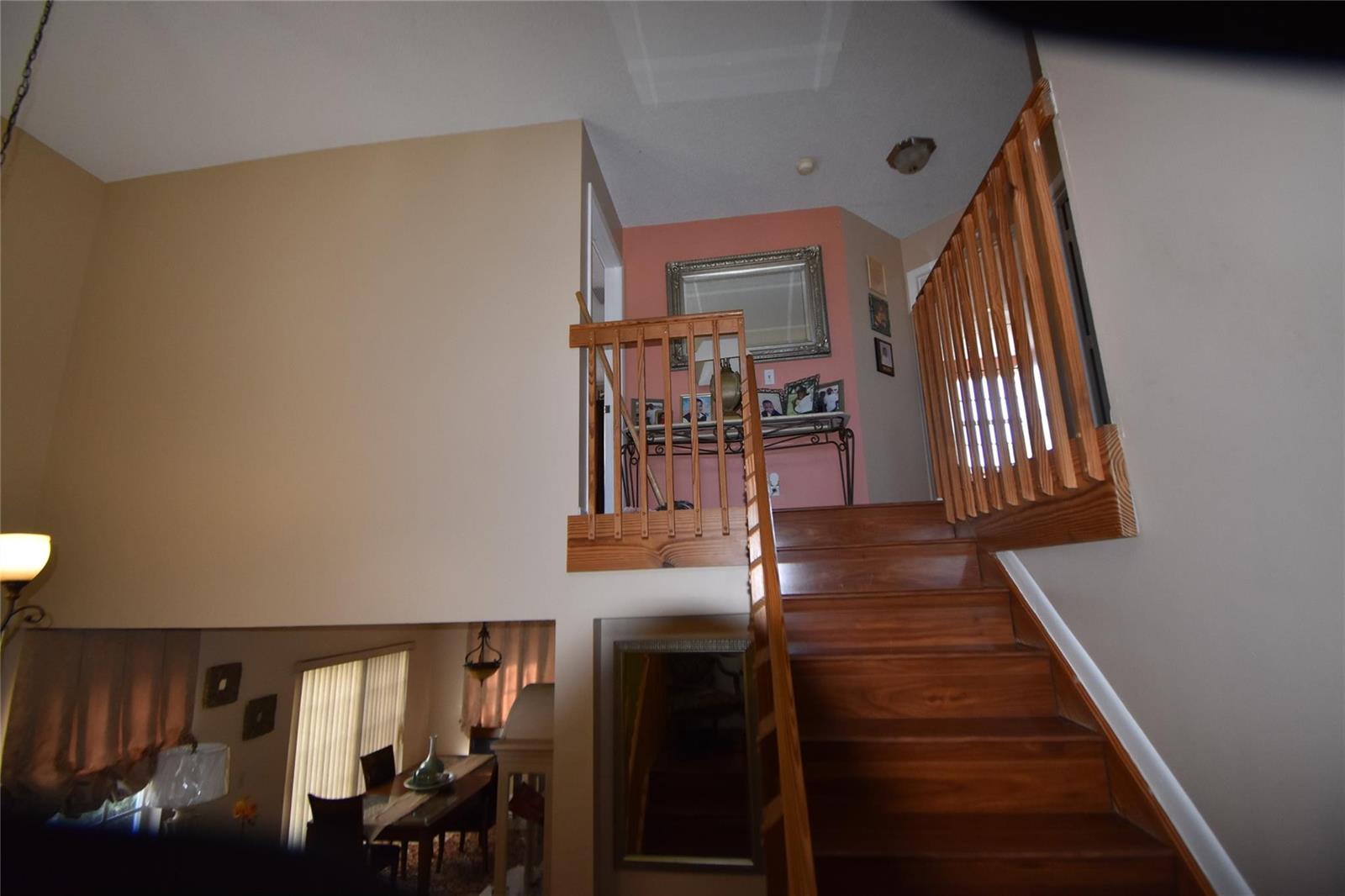A wooden staircase leads to a landing with a coral-colored wall and a mirror — 6572 Bayfront Drive, Margate FL 33063, MARGATE, FL