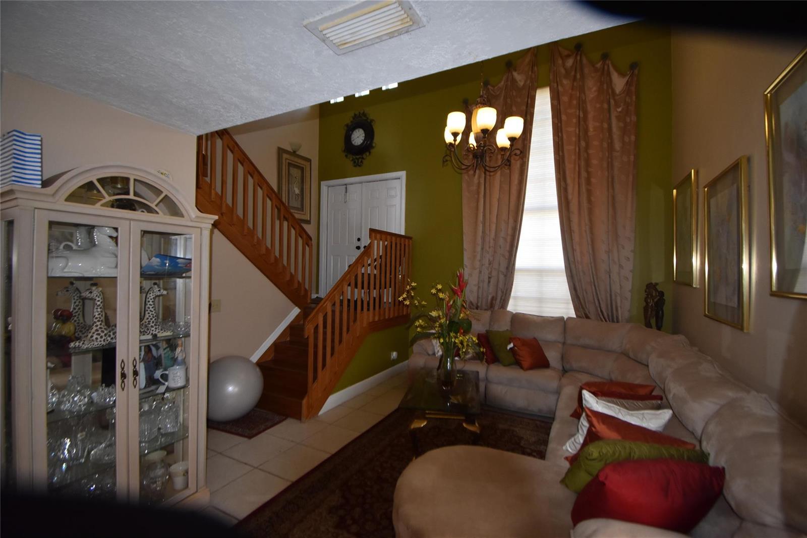 A living room features a sectional sofa, a staircase, and a tall window with curtains — 6572 Bayfront Drive, Margate FL 33063, MARGATE, FL