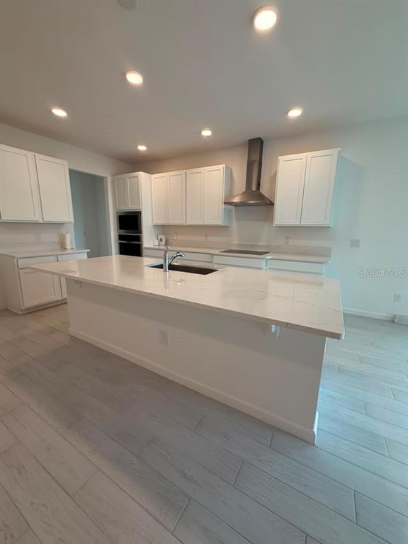 A modern kitchen features white cabinetry, a large quartz-topped island, and light wood-look tile flooring — 5197 PRAIRIE PRESERVE RUN, ST CLOUD, FL