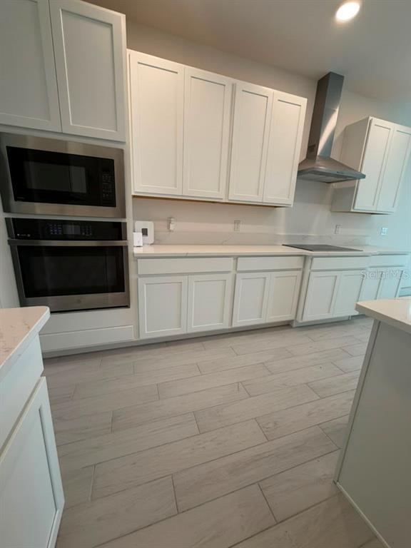 A modern kitchen features white cabinets, stainless steel appliances, and light wood-look tile flooring — 5197 PRAIRIE PRESERVE RUN, ST CLOUD, FL