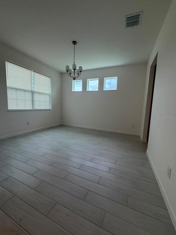 An empty dining room features light wood-look tile flooring, a chandelier, and three small windows — 5197 PRAIRIE PRESERVE RUN, ST CLOUD, FL