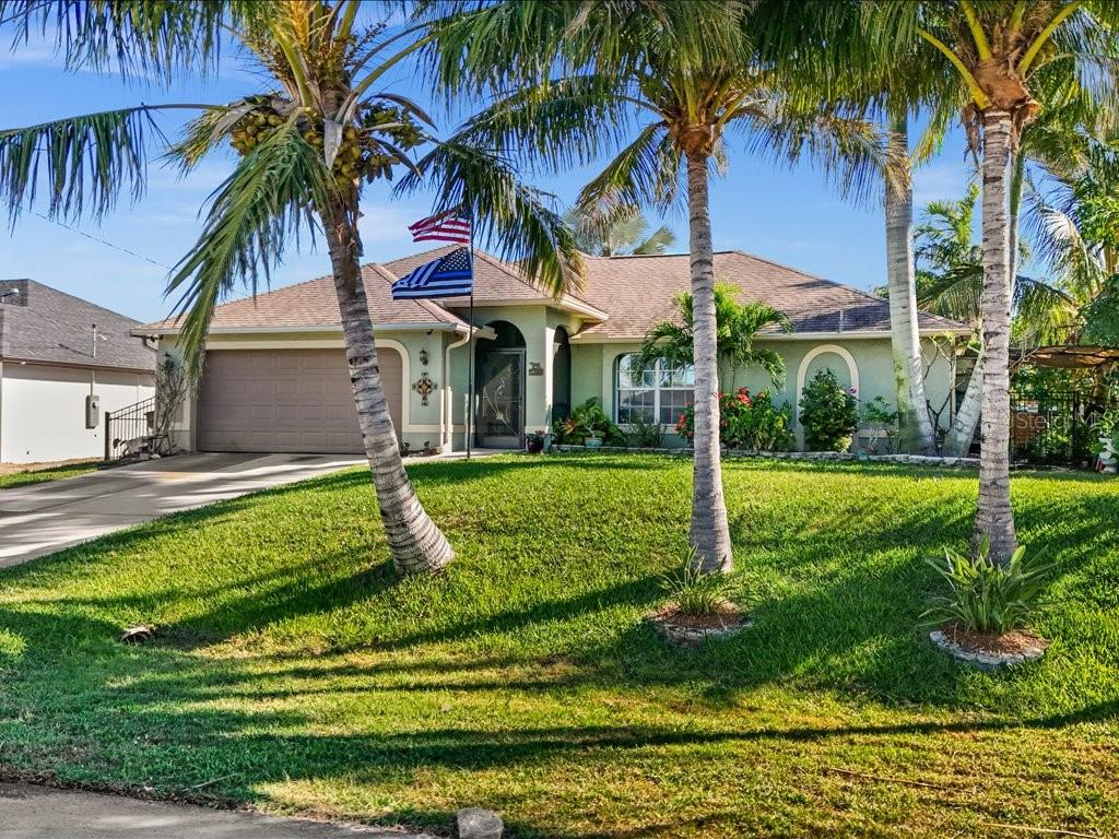 A single-story house with a garage, palm trees, and two flags in the front yard — 1209 NW 25TH PLACE, CAPE CORAL, FL
