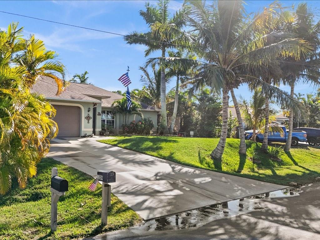 A single-story house with a concrete driveway, palm trees, and an American flag in front — 1209 NW 25TH PLACE, CAPE CORAL, FL