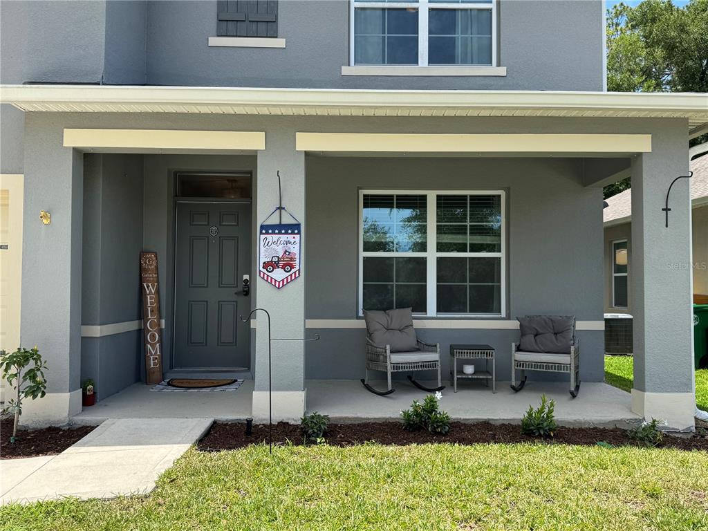 A gray two-story house features a covered front porch with rocking chairs and a welcome sign — 325 CHARLES DRIVE, DELAND, FL