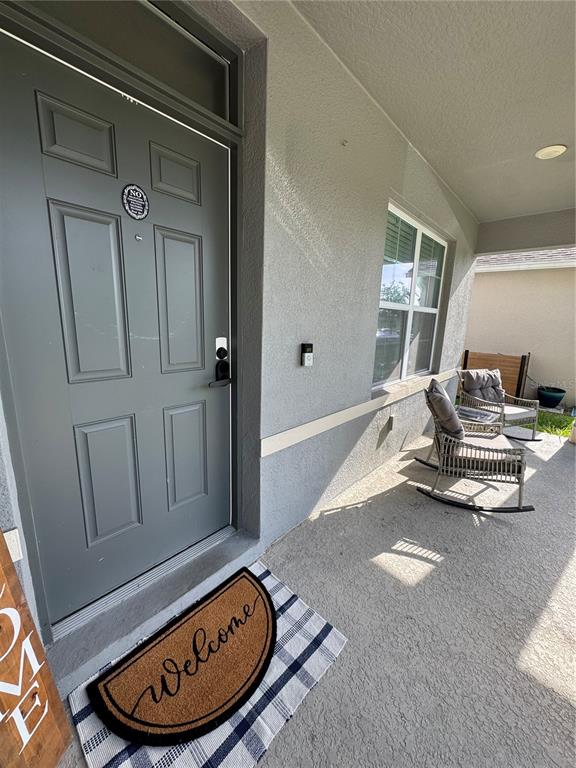 A gray front door with a welcome mat opens onto a covered concrete porch — 325 CHARLES DRIVE, DELAND, FL
