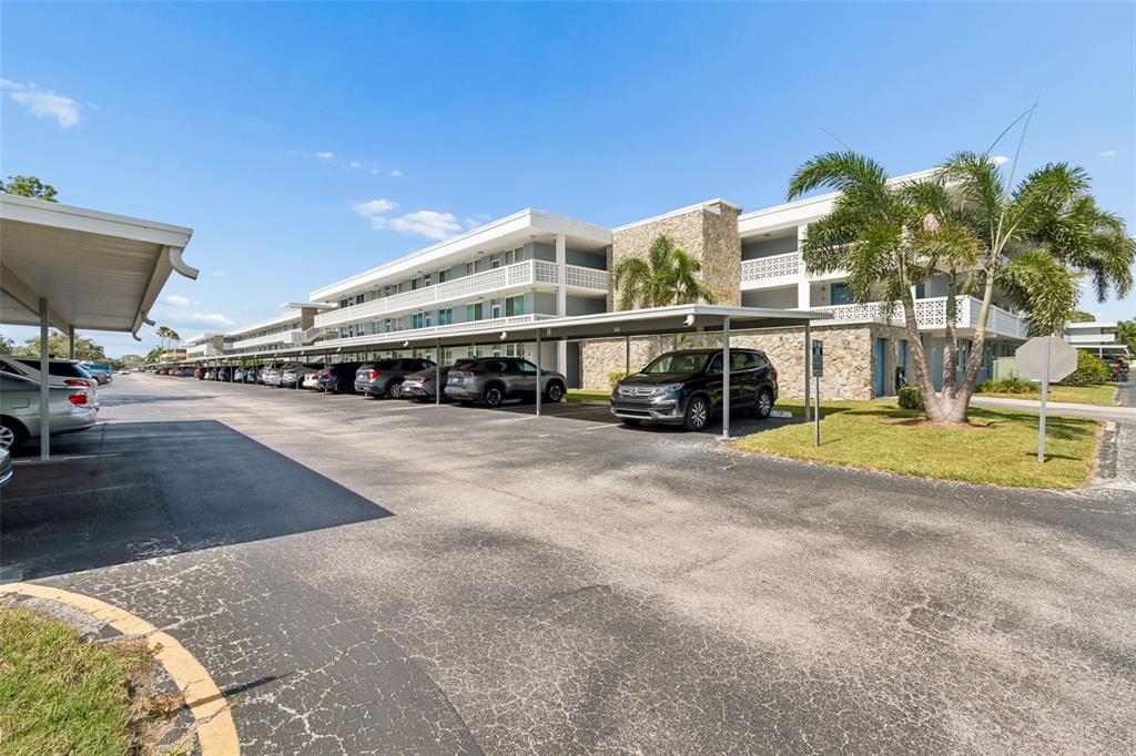 A multi-story apartment building features a stone facade, covered parking, and palm trees — 4715 BAY STREET NE UNIT 223, ST PETERSBURG, FL
