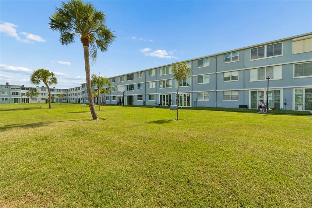 A large grassy lawn sits in front of a multi-story blue apartment building — 4715 BAY STREET NE UNIT 223, ST PETERSBURG, FL