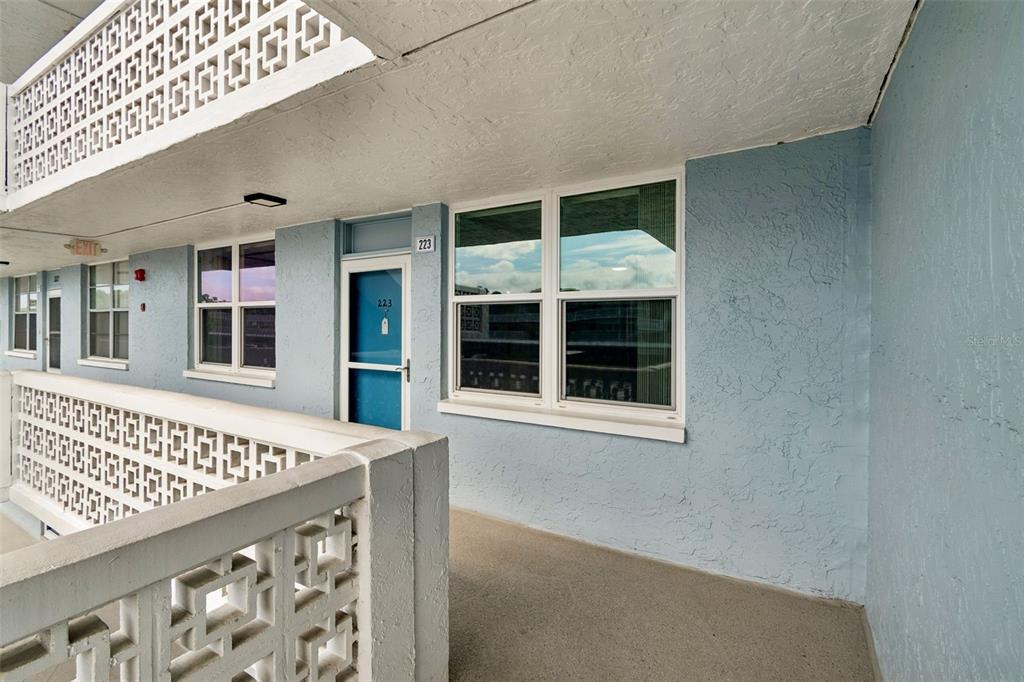 An exterior walkway with a blue door, white windows, and decorative concrete railings — 4715 BAY STREET NE UNIT 223, ST PETERSBURG, FL