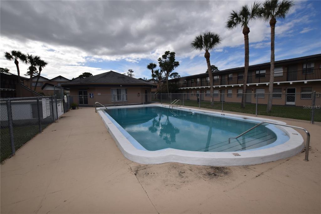 An outdoor swimming pool is surrounded by a concrete deck, chain-link fencing, and apartment buildings — 1713 DIXON BOULEVARD UNIT 159, COCOA, FL