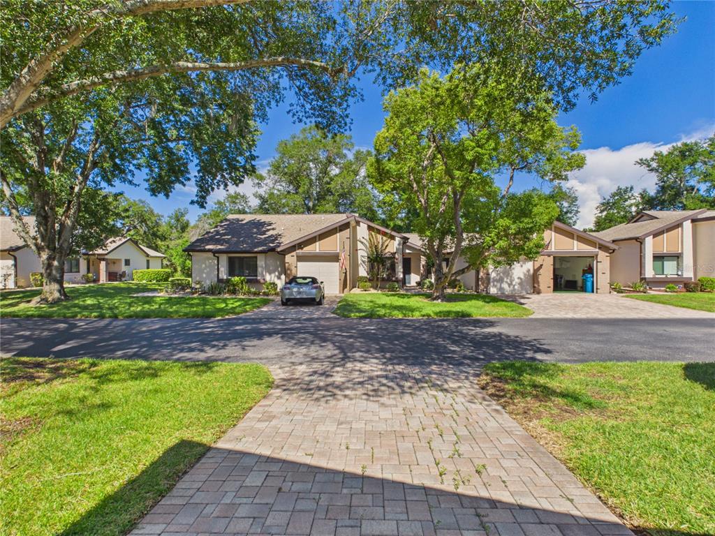 A view of a single-story residential building with a paved driveway and mature trees — 7511 HEATHER WALK DRIVE, WEEKI WACHEE, FL