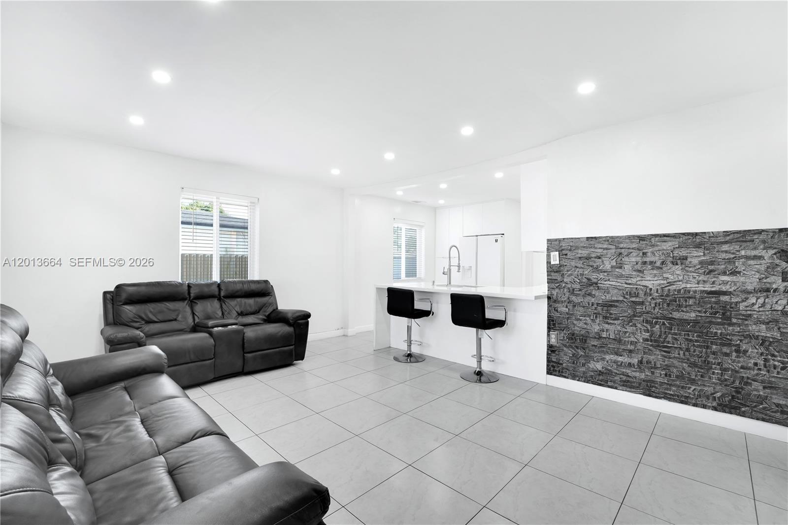 A living room and kitchen area feature white walls, tile flooring, and a stone accent wall — 9425 NW 36th Ave, Miami FL 33147, MIAMI, FL