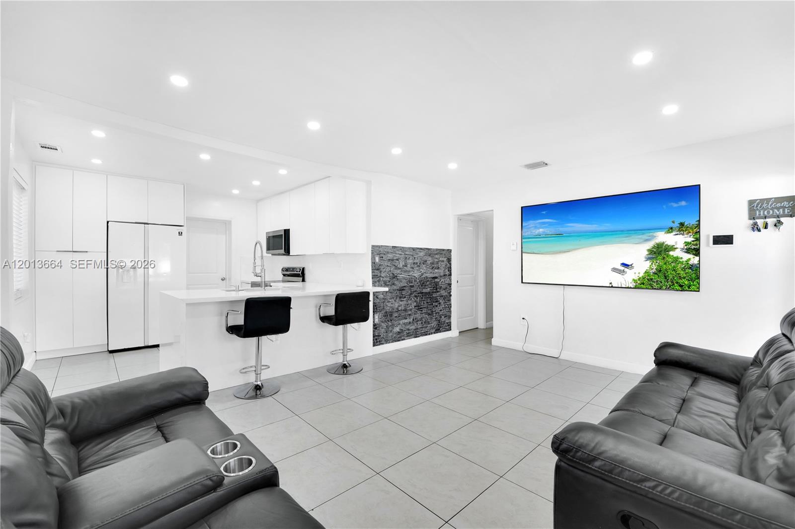 A modern open-concept living room and kitchen featuring white cabinetry, tile flooring, and leather sofas — 9425 NW 36th Ave, Miami FL 33147, MIAMI, FL