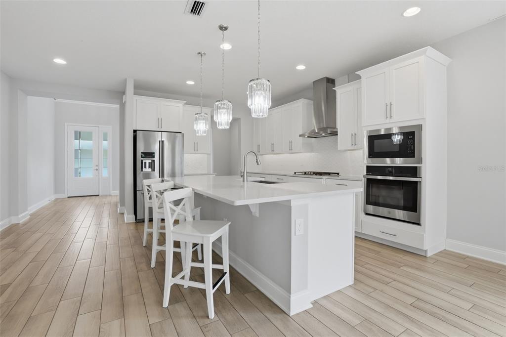 A modern kitchen features white cabinetry, a central island with bar stools, and light flooring — 13978 LANYARD WAY, WINTER GARDEN, FL