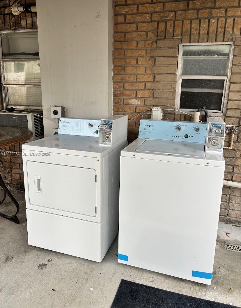 Two white coin-operated Whirlpool laundry machines sit on a concrete patio against a brick wall — 117 NE 5TH ST NE # 113, Winter Haven FL 33881, WINTER HAVEN, FL