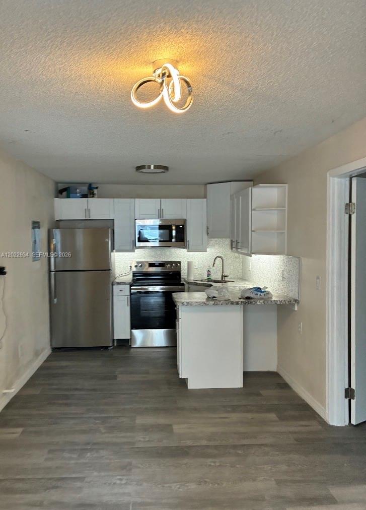 A kitchen features white cabinets, stainless steel appliances, and gray wood-look flooring — 117 NE 5TH ST NE # 113, Winter Haven FL 33881, WINTER HAVEN, FL