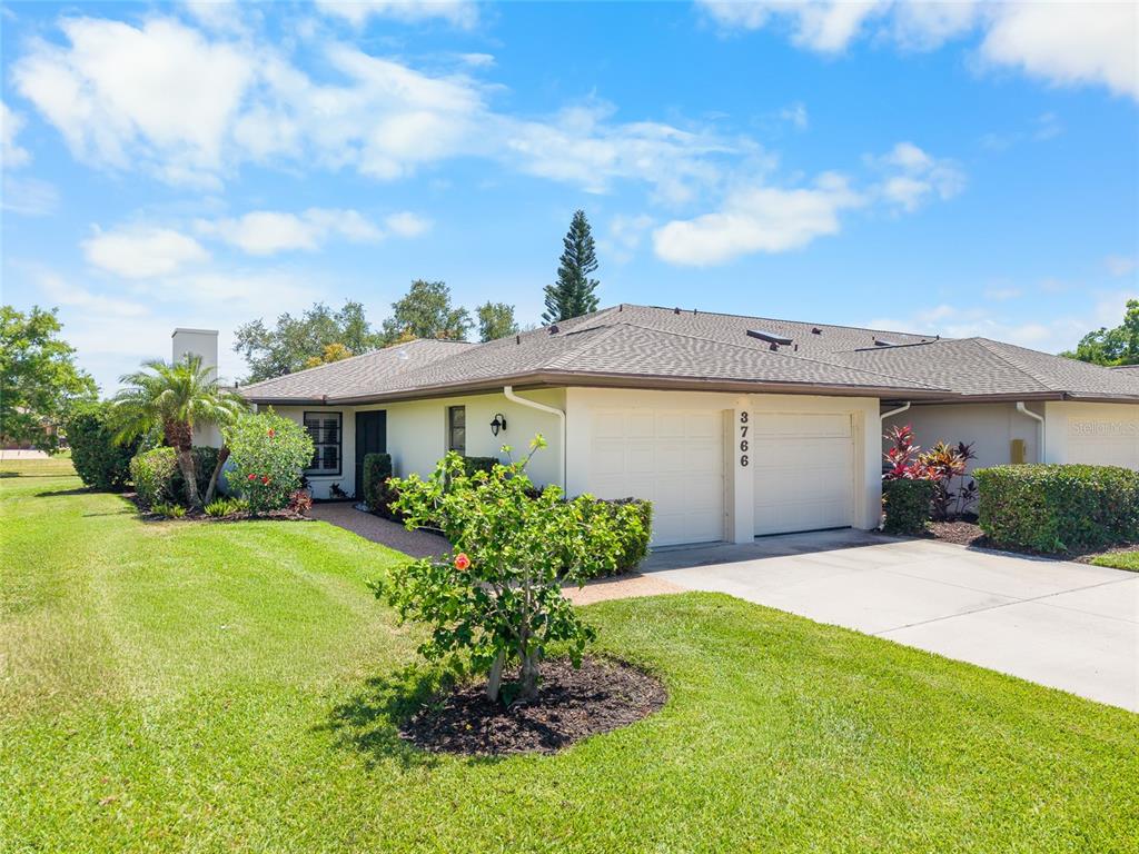 A single-story house with a two-car garage, a lawn, and landscaping under a blue sky — 3766 BALLANTRAE DRIVE UNIT 22D, SARASOTA, FL